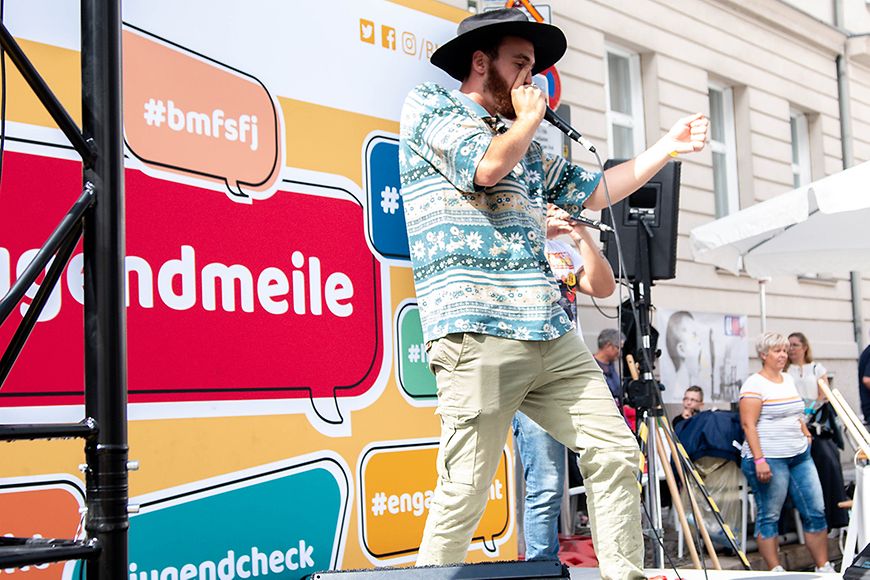 Ein Musiker spielt auf einer Bühne, im Hintergrund der Banner "Jugendmeile"
