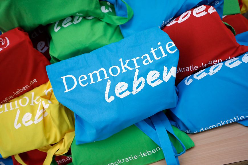 Blaue, rote, grüne und gelbe Tragetaschen des Projekts "Demokratie leben"