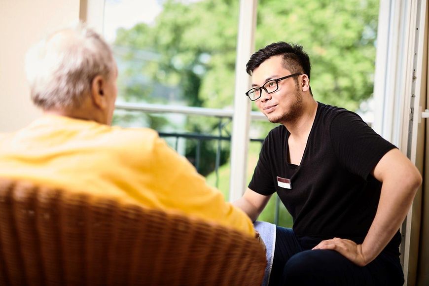 Eine Pflegekraft wendet sich einem älteren Mann mit Demenz zu 