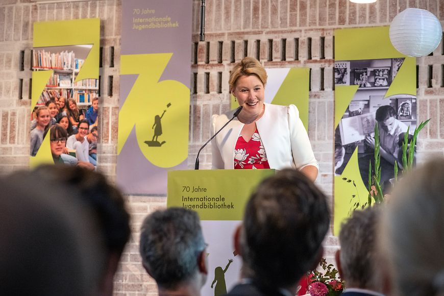 Dr. Franziska Giffey am Redepult vor einer Wand mit der Aufschrift 70 Jahre Internationale Jugendbibliothek