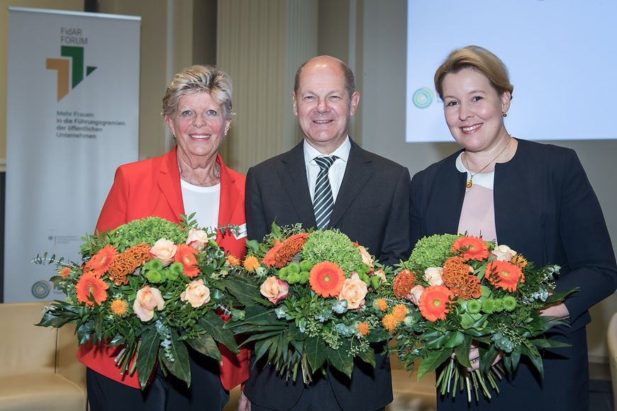 Drei Personen mit Blumensträußen in den Händen vor einem Aufsteller mit der Aufschrift Fidar-Forum