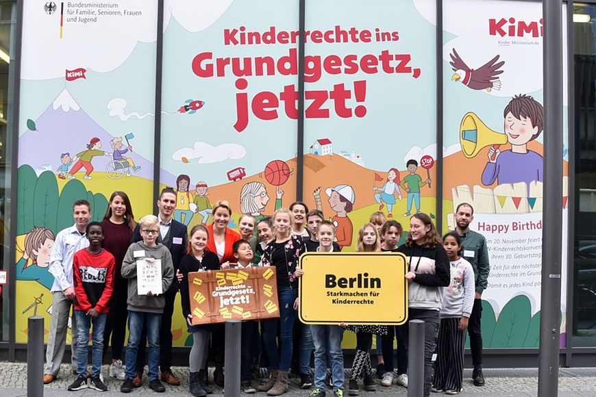 Kinder und Jugendliche vor dem Bundesfamilienministerium und einem Plakat mit der Aufschrift: Kinderrechte ins Grundgesetz!