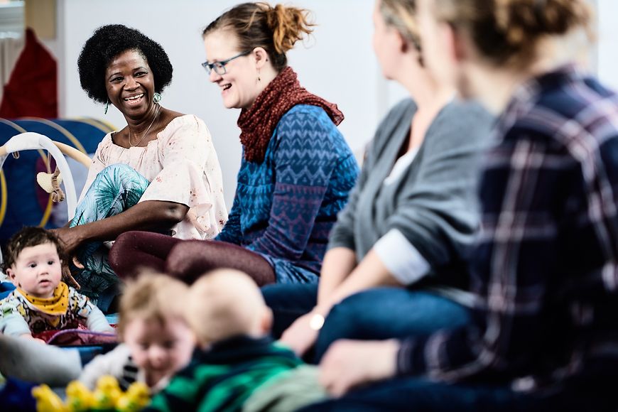 Mehrere Mütter und Kinder sitzen lachend in einer Gruppe zusammen