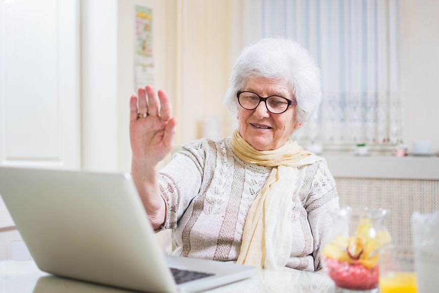 Grauhaarige Seniorin winkt in ihren Laptop