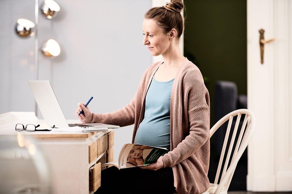 Eine schwangere Frau sitzt am Schreibtisch und arbeitet