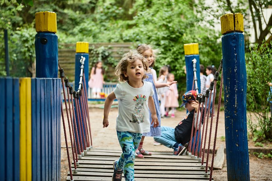 Ein Kind läuft in einer Kita im Freien über eine Brücke