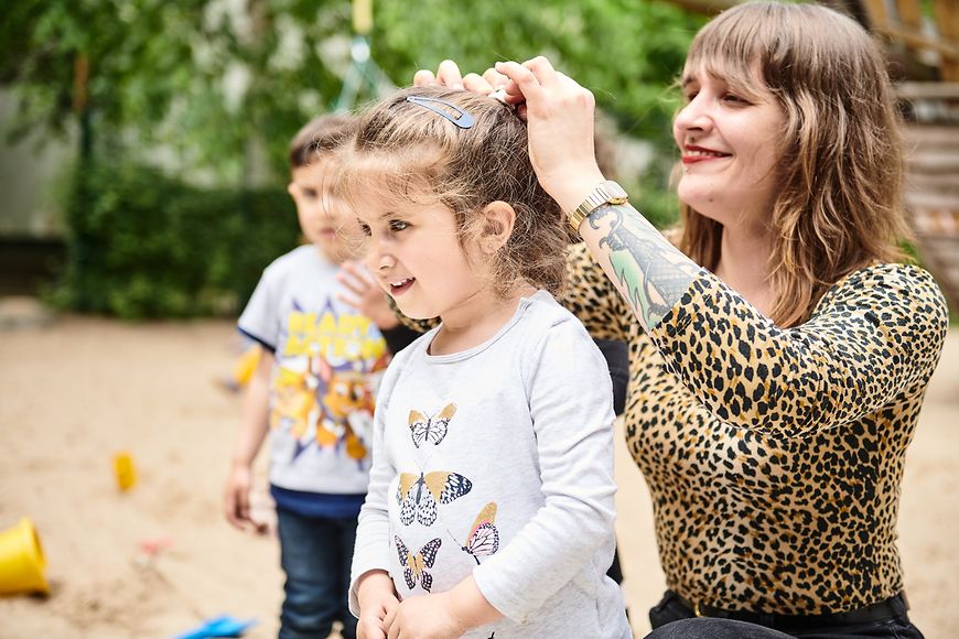 Ein Frau macht auf einem Spielplatz die Haare von einem Kind