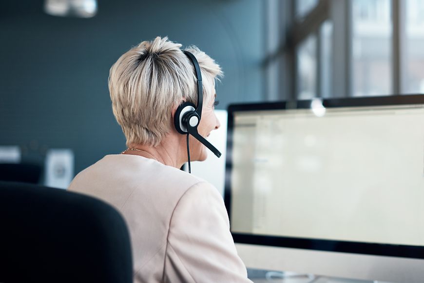 Eine Frau sitzt mit einem Headset an einem Computer