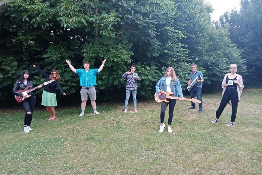 Junge Frauen und Männer stehen mit und ohne Instrumente auf einer Wiese