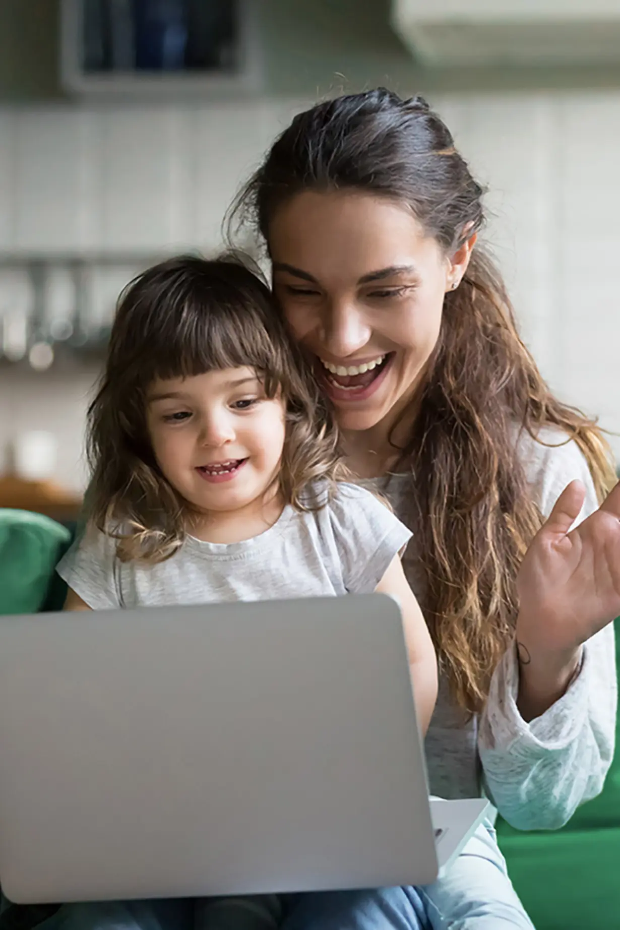 Eine Mutter sitzt mit ihrer kleinen Tochter lachend vor einem Laptop