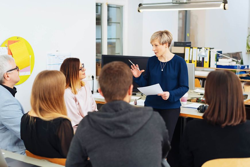 Eine Frau wendet sich erklärend an eine Gruppe aus fünf Menschen 