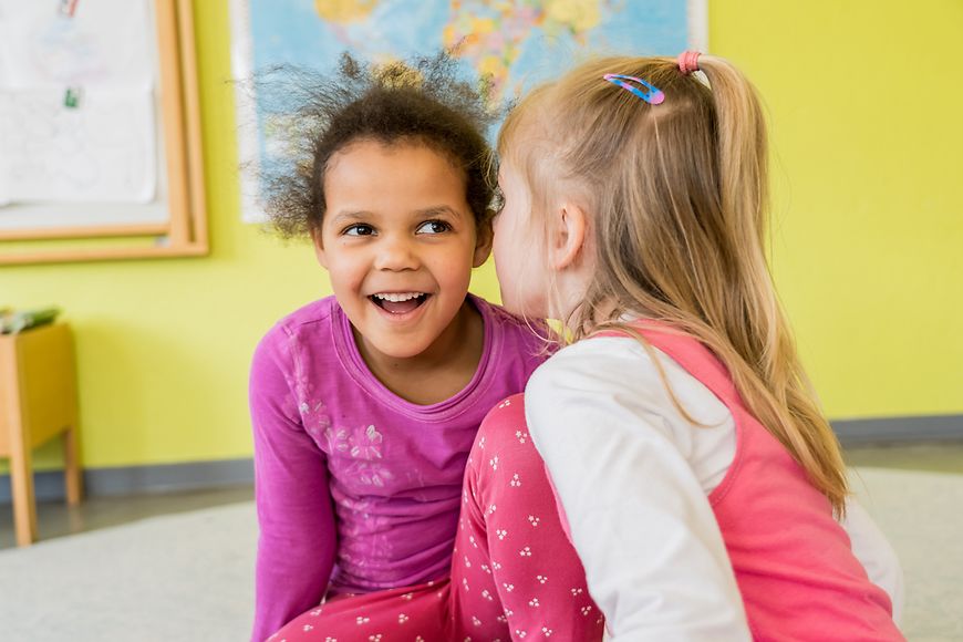 Zwei Kinder in einer Kita flüstern sich etwas zu