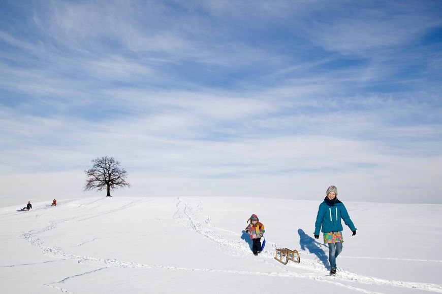Mutter und Kind beim Rodeln an einem Berg im Urlaub