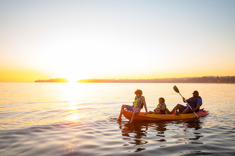 Das Bild zeigt eine Familie im Urlaub im Paddelboot auf einem See