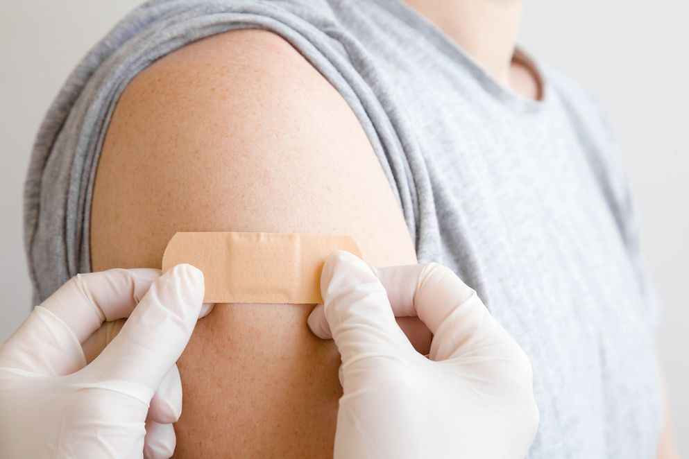 Ein Arzt klebt nach der Impfung ein Pflaster auf einen Arm