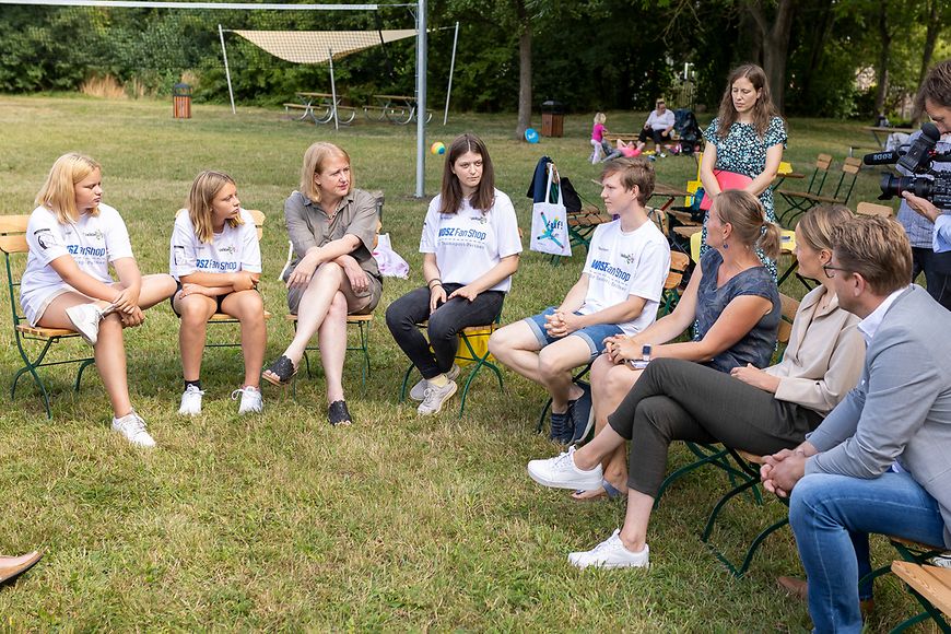 Lisa Paus sitzt draußen auf einer Grünfläche zusammen mit Jugendlichen