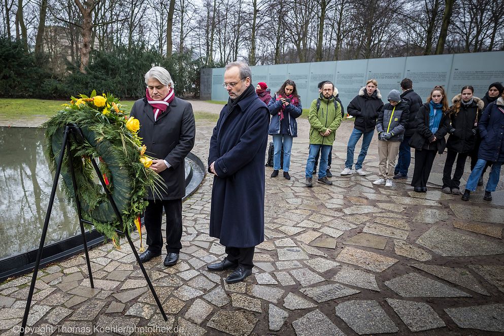 Dr. Mehmet Daimagüler und Dr. Felix Klein stehen vor einem Kranz und gedenken der getöteten Sinti und Roma