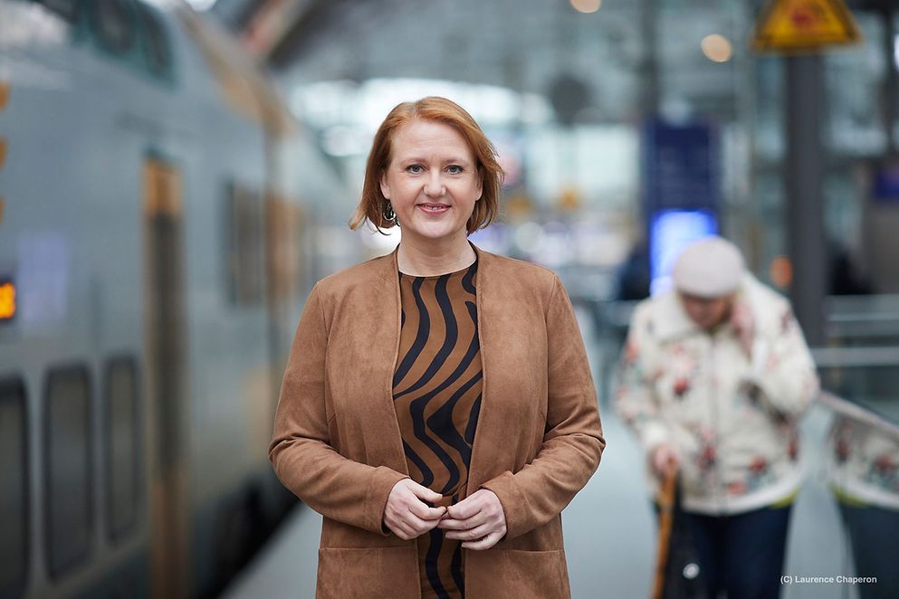 Lisa Paus steht auf einem Bahnhof. Im Hintergrund ist eine ältere Frau zu sehen