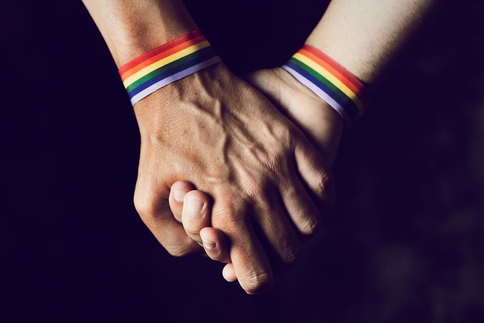 Zwei Menschen mit Armband in Regenbogenfarben nehmen sich an die Hand 