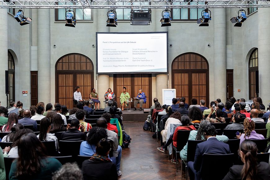 Teilnehmende der Veranstaltung. Blick auf Bühne mit Leinwand