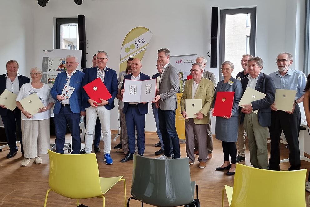 Sven Lehmann steht in einer Gruppe und zeigt die neuen Jugendmarken 
