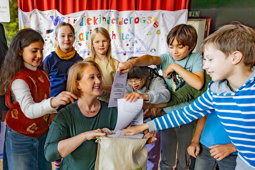 Lisa Paus hält einen Rucksack, in den Kinder Zettel stecken.