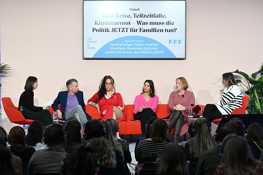 Lisa Paus sitzt mit anderen Diskussionsteilnehmenden auf einem Podium. Vor ihr sitzt das Publikum.