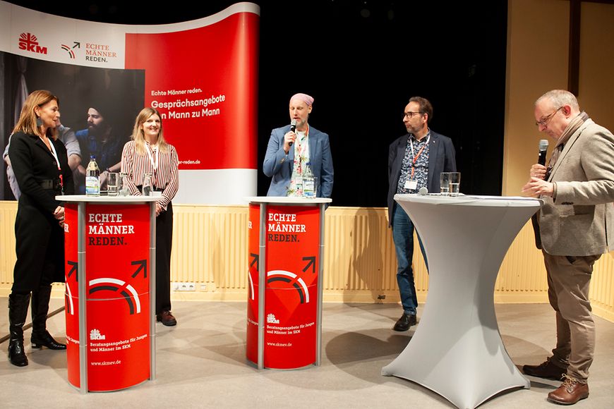 Fünf Personen stehen im Halbkreis an Rednerpulten und unterhalten sich.