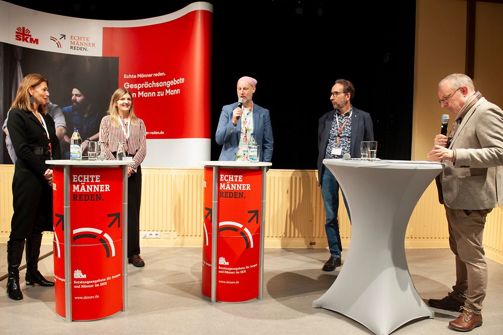 Fünf Personen stehen im Halbkreis an Rednerpulten und unterhalten sich.