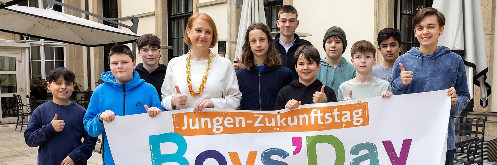 Lisa Paus und eine Gruppe Jugendlicher stehen vor einem Boys-Day-Banner