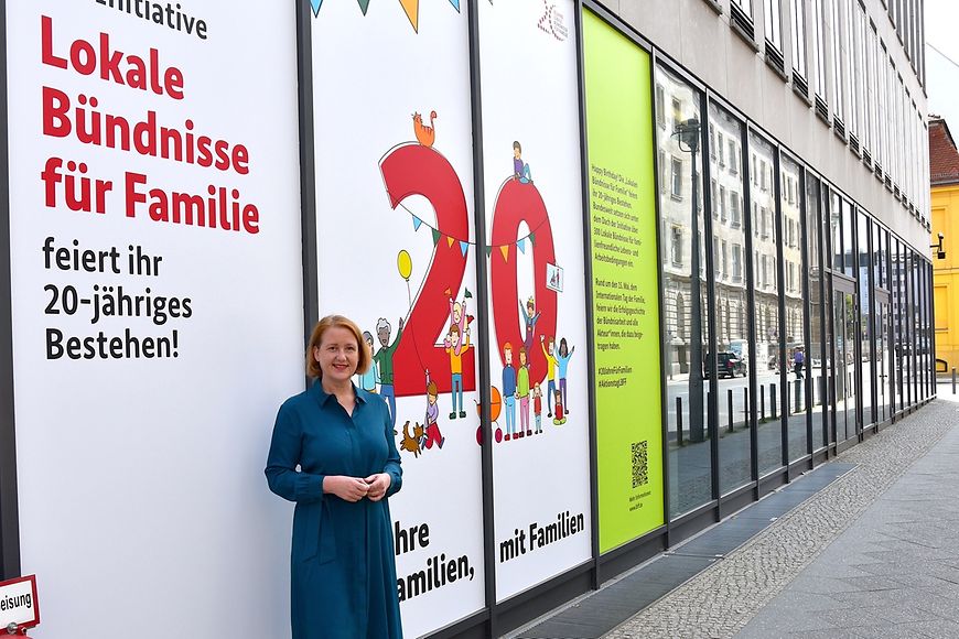 Lisa Paus steht vor der Fassade des Bundesfamilienministeriums, auf der Glückwünsche zum Jubiläum zu lesen sind