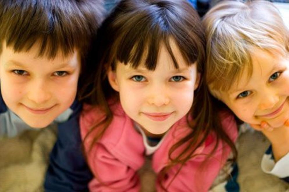 Ein lächelndes Mädchen wird umringt von zwei Jungen, die in die Kamera lachen. Bildquelle: iStock