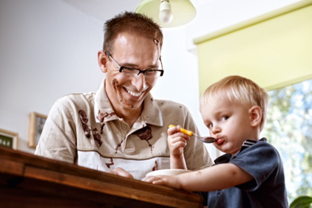 Ein Vater hilft seinem Kind beim Essen eines Schokopuddings. Bildquelle: Erfolgsfaktor Familie