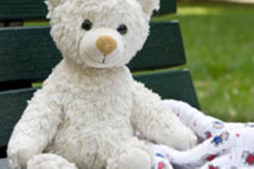 Ein weißer Teddybär sitzt auf einer grünen Parkbank