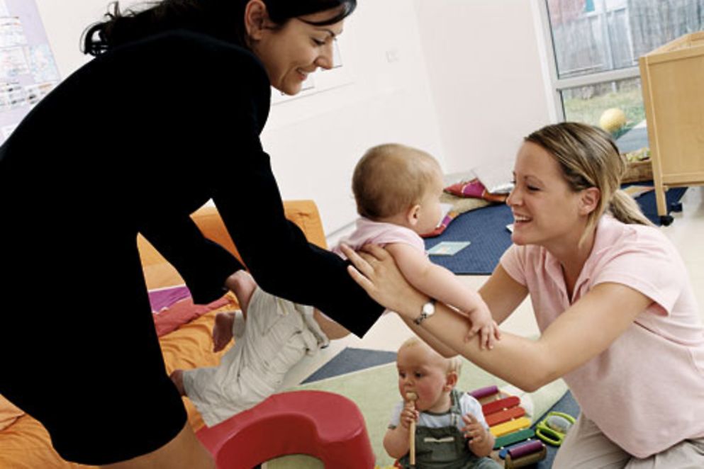 Eine Mutter übergibt ihre Kinder einer Betreuerin in einer Kita.