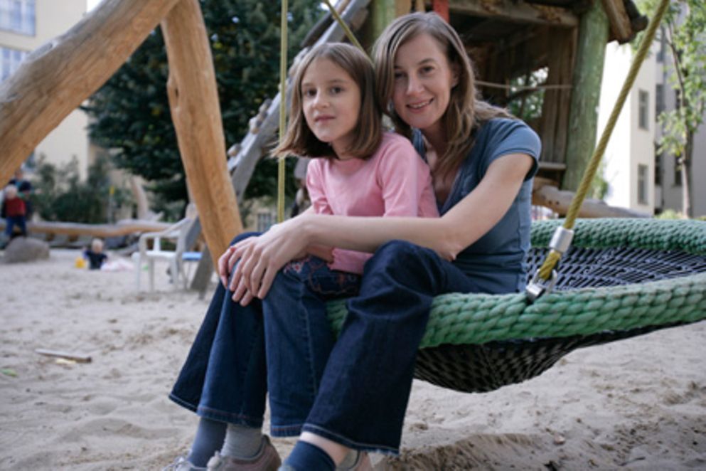 Eine Mutter sitzt mit ihrer Tochter im Arm auf einem Spielplatz, Bildnachweis: Müttergenesungswerk