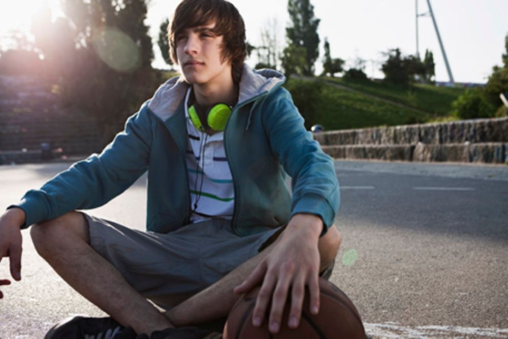 Ein Jugendlicher sitzt auf einem Basketballplatz und hört Musik. Bildquelle: Colourbox.com