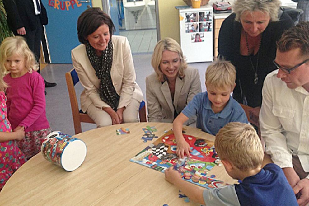 Manuela Schwesig und Malu Dreyer sitzen mit Kindern am Tisch einer Betriebskita der Schott AG