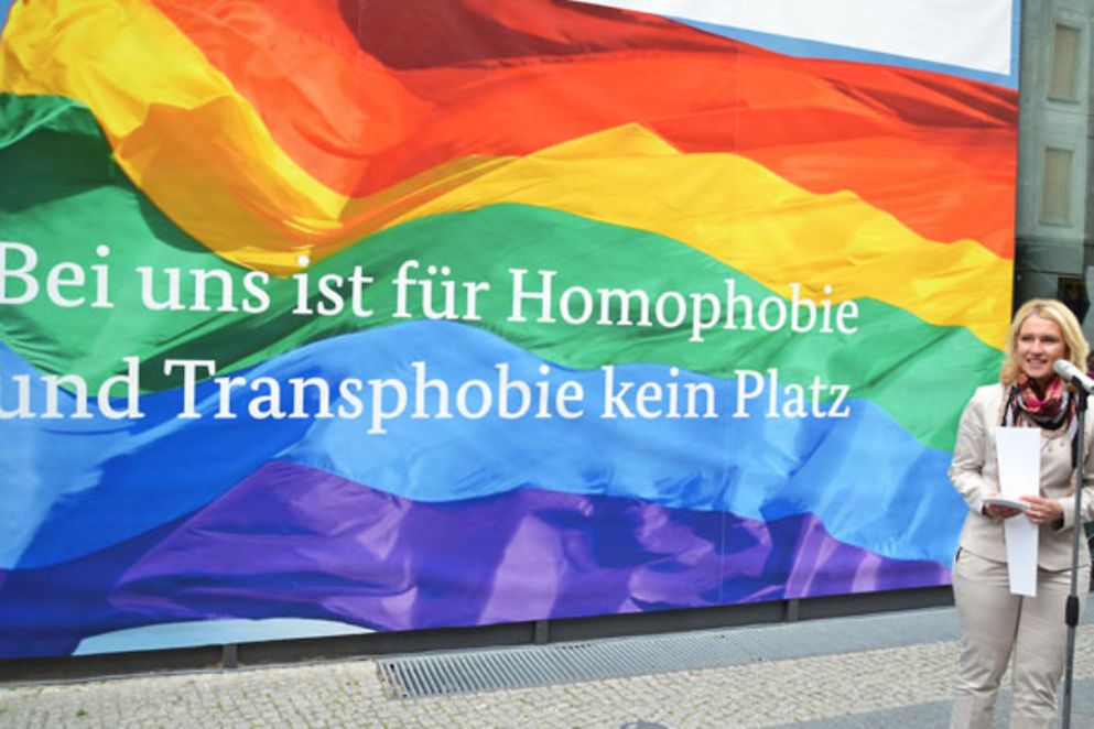 Manuela Schwesig präsentiert das Plakat gegen Homophobie und Transphobie vor dem Berliner Familienministerium