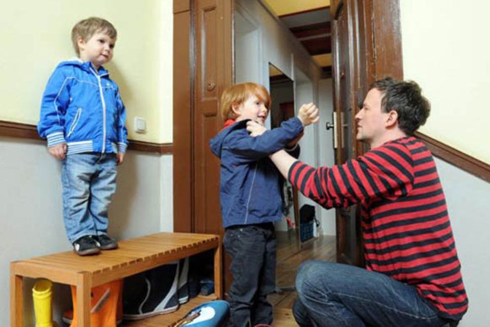 Ein Vater zieht seinen zwei Kindern die Jacke an.