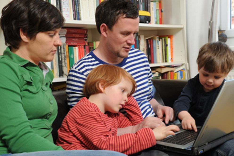 Eine Familie sitzt am Laptop und sieht sich einige Informationen im Internet an
