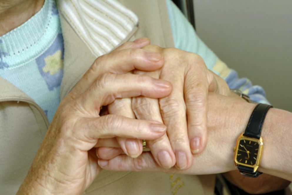 Die Hände einer älteren Frau umfassen die Hand einer jüngeren.