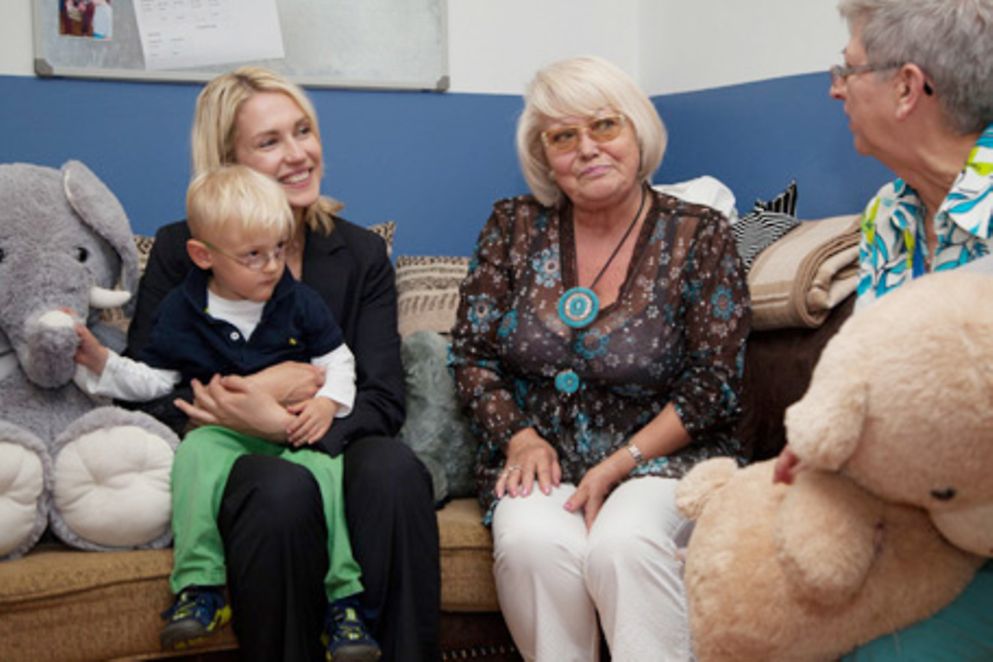 Manuela Schwesig sitzt mit einem klienen Jungen und der Leiterin auf einer Couch in einem Mehrgenerationenhaus in Fürth.