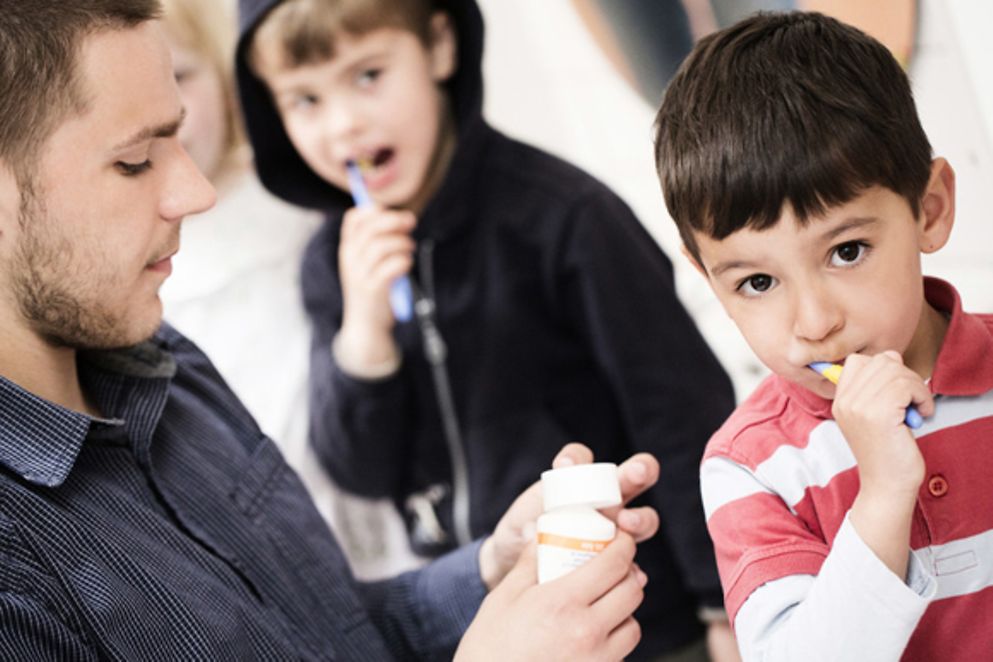 Jungendlicher hilt Kindern beim Zähneputzen