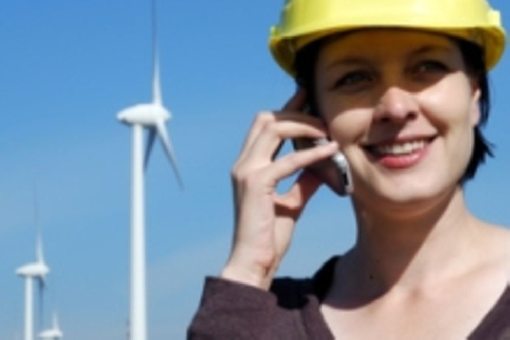 junge Frau mit Schutzhelm steht vor Windrädern und telefoniert