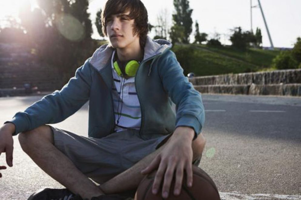 Ein Teenager sitzt mit einem Basektball auf dem Asphalt