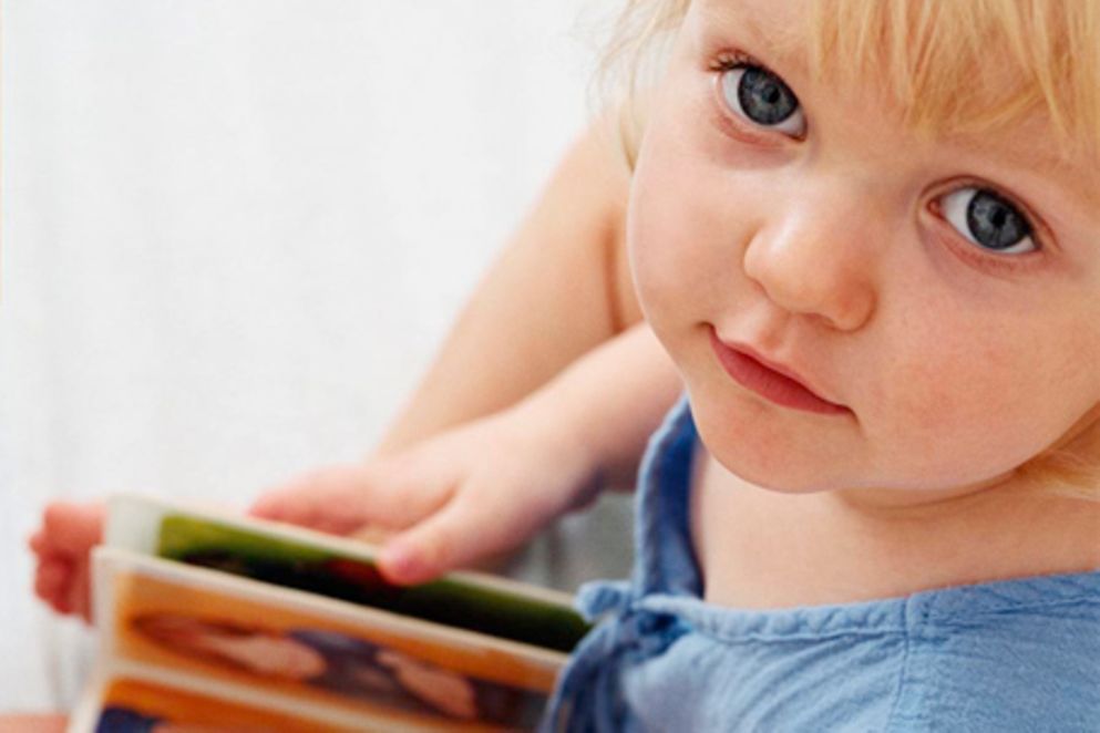 Ein kleines Kind hält ein Buch und blickt in die Kamera.