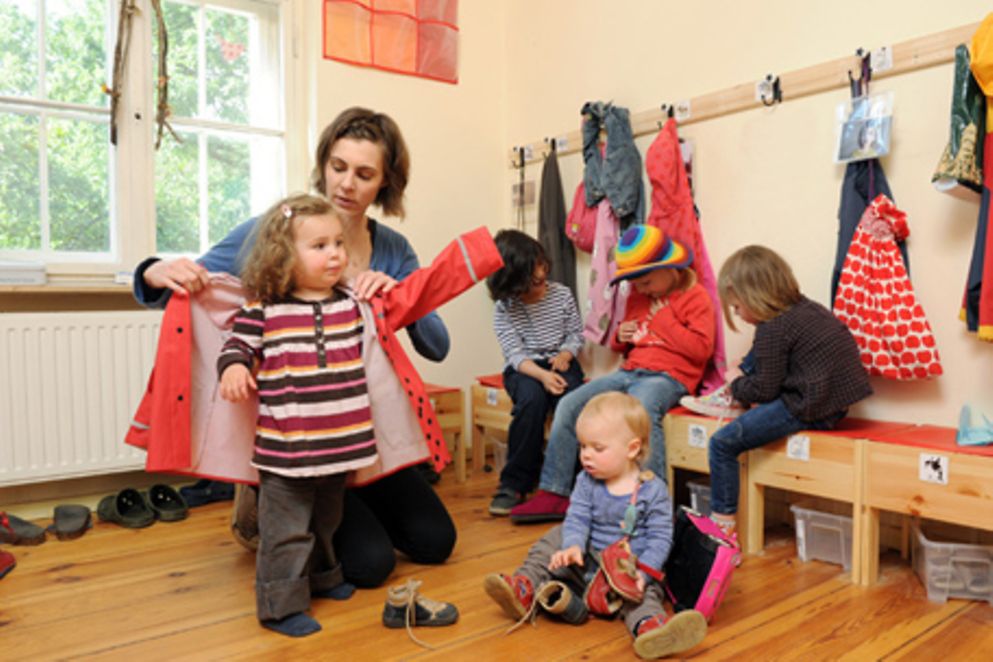 Eine Betreuerin hilft fünf Kindern beim Anziehen von Jacken und Schuhen. Bildquelle: M. Gronau / BMFSFJ