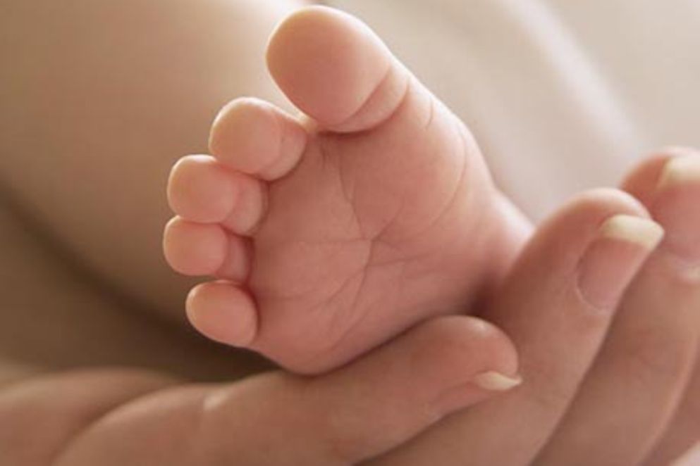 Eine junge Frau hält den Fuß eines Babys in ihrer Hand.
