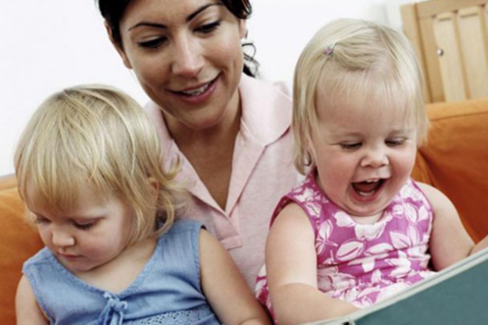 Eine junge Mutter liest mit ihren beiden Töchtern in einem Bilderbuch.